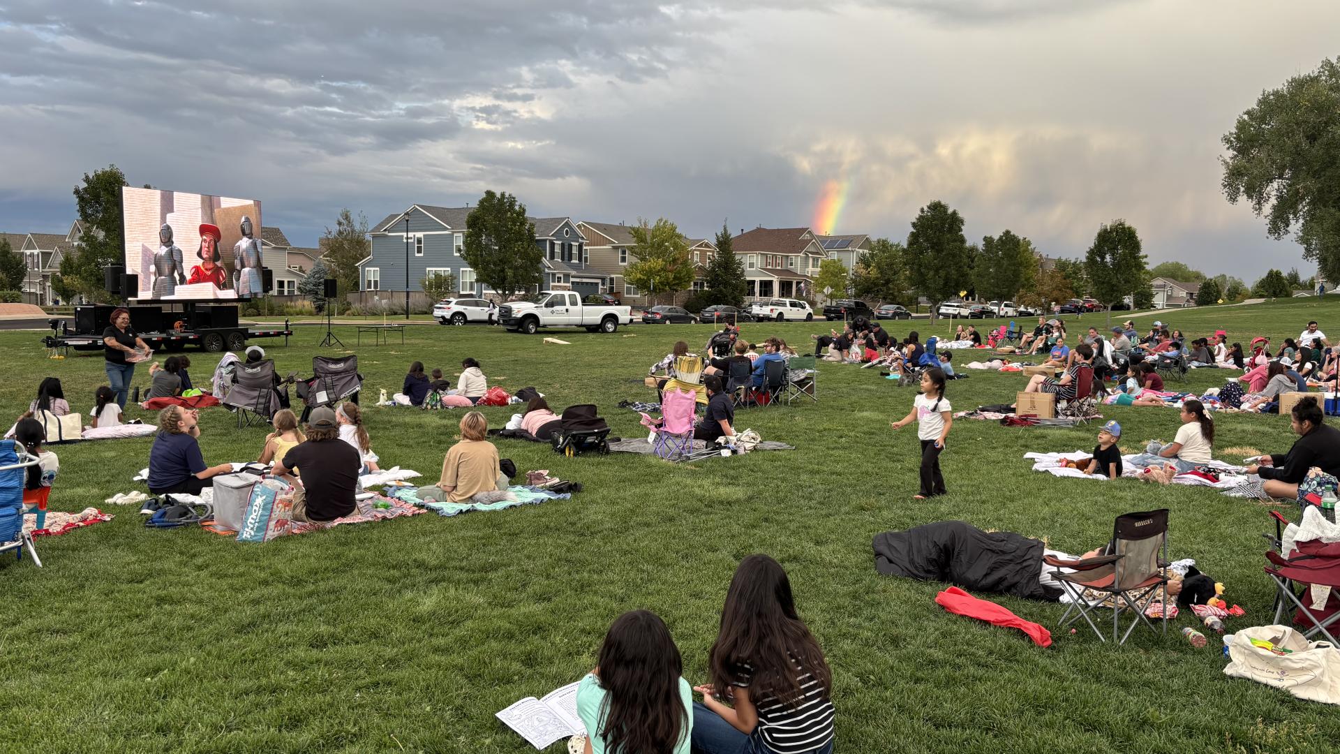 families sitting on the grass watching a movie on a projector screen