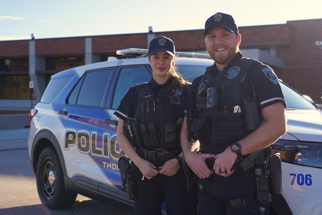 Two officers in front of a patrol car smiling